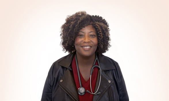 A smiling woman wearing a dark jacket and a stethoscope around her neck.