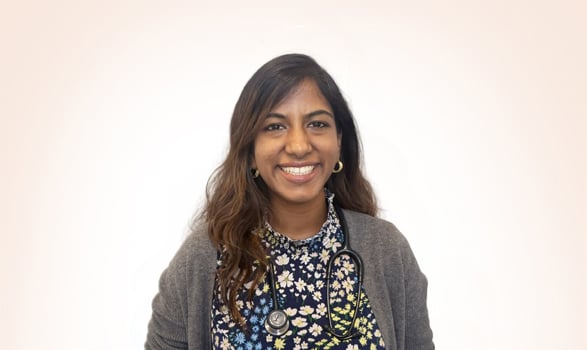 A smiling woman wearing a floral shirt, gray cardigan, and a stethoscope around her neck.